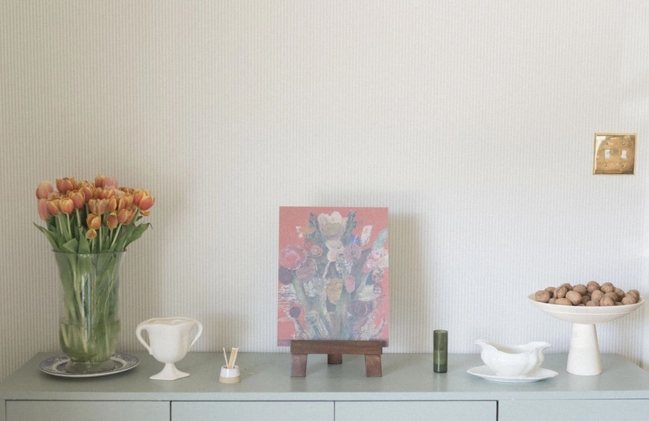 Decorative setting with a vase of flowers, a painting on an easel, and small items on a surface.