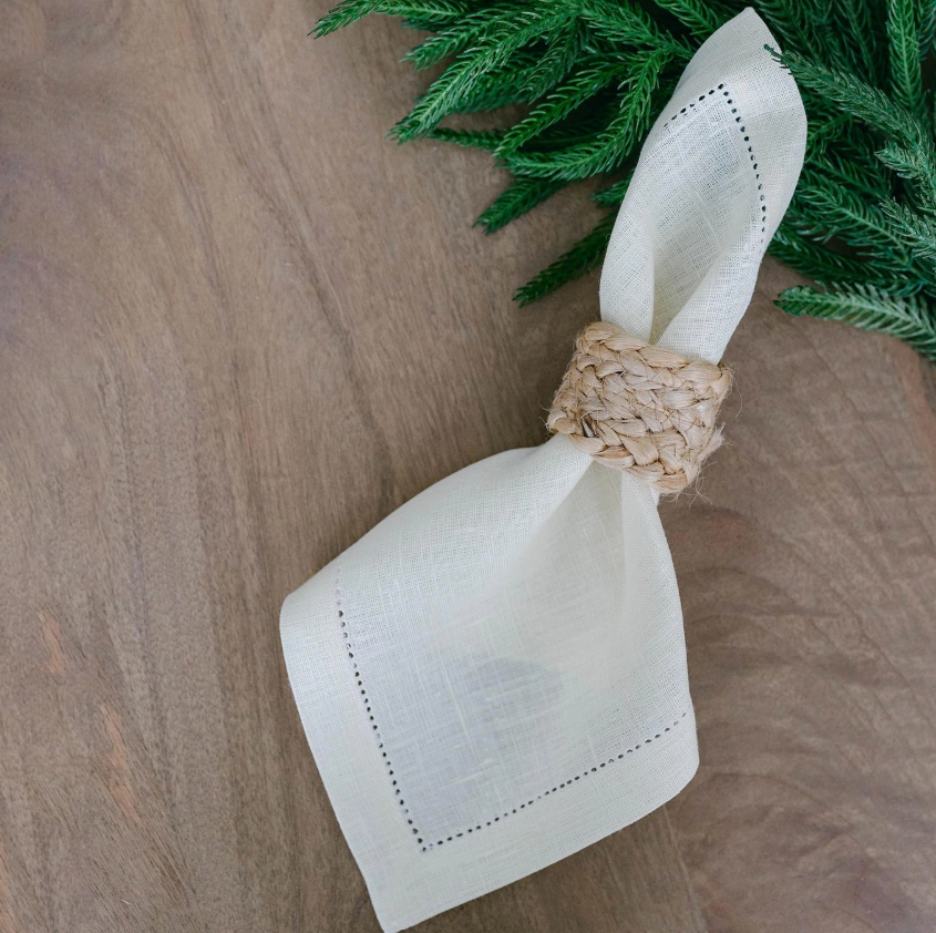White napkin with a woven ring on a wooden surface with greenery