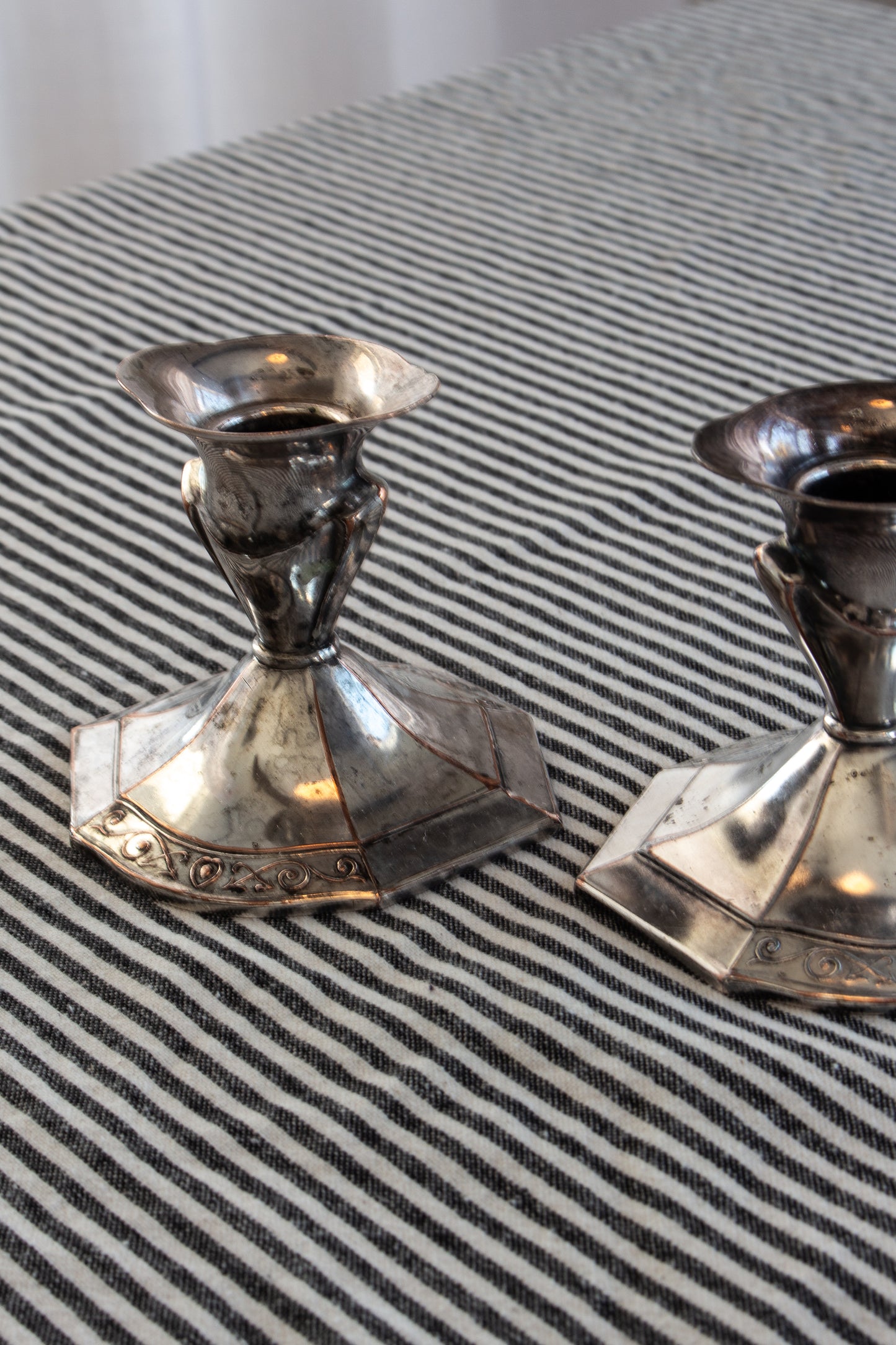 Two silver candle holders on a striped fabric background
