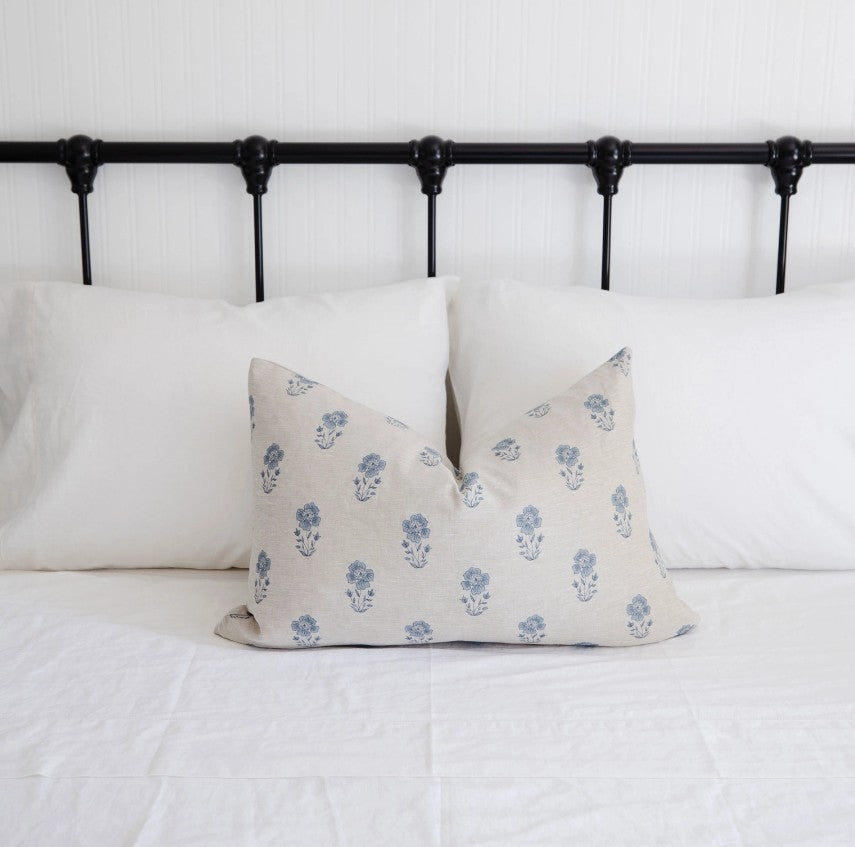 Floral patterned pillow on a bed with a black metal headboard.