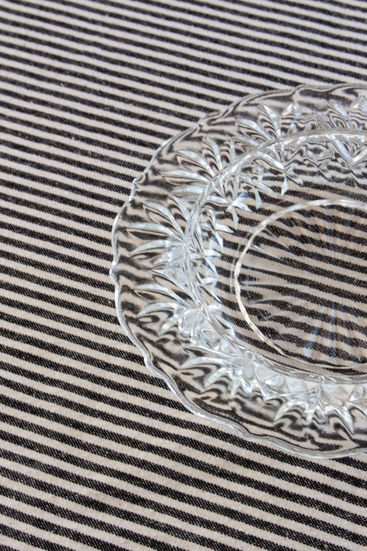 Clear glass plate with decorative edge on a striped fabric background