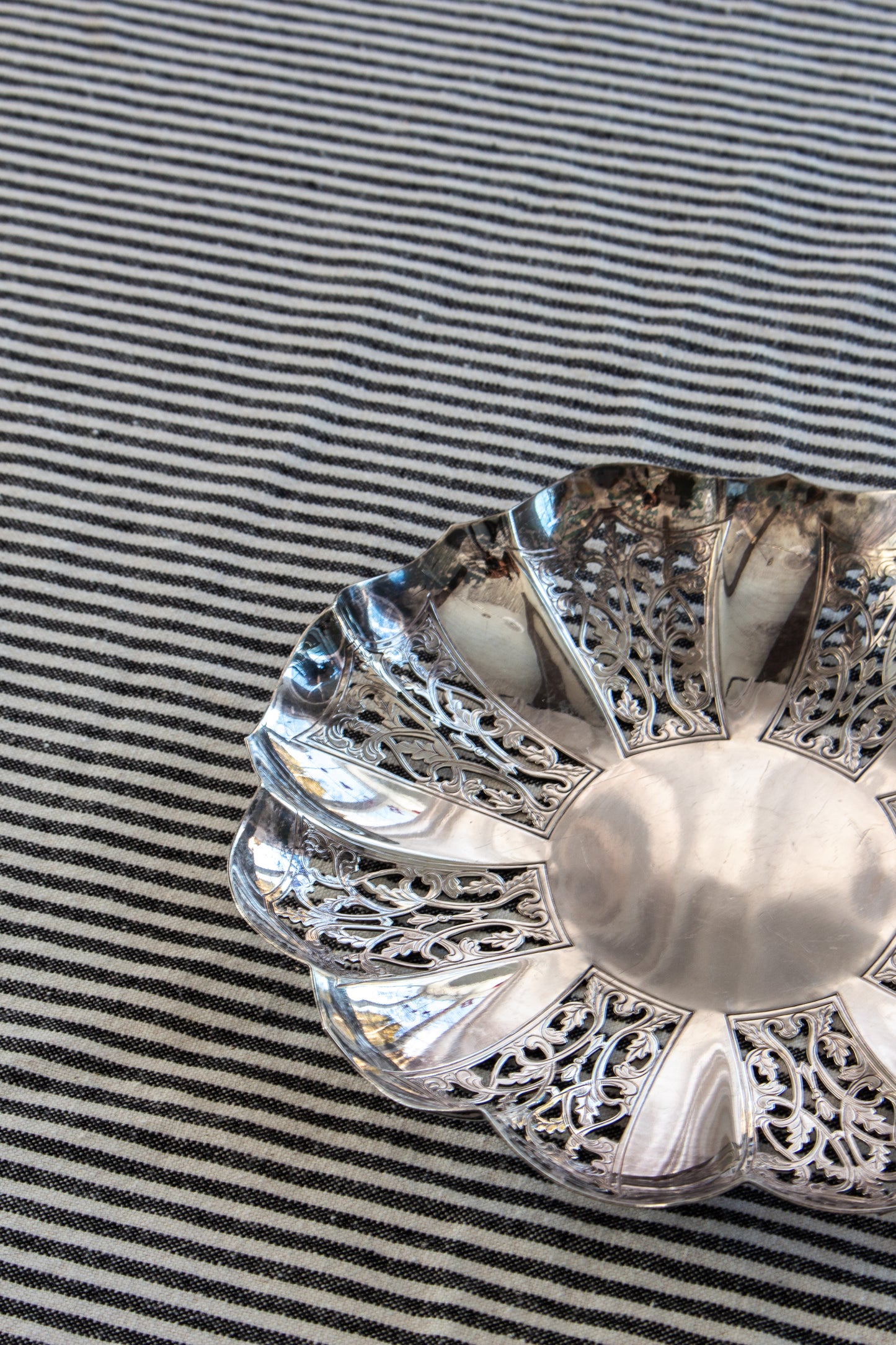 Decorative silver dish with intricate patterns on a striped fabric background