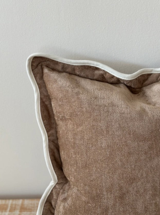 Brown textured pillow with white piping on a neutral background