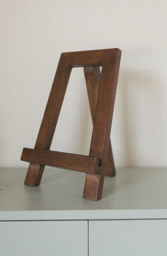 Wooden easel on a light gray surface with a white textured wall background