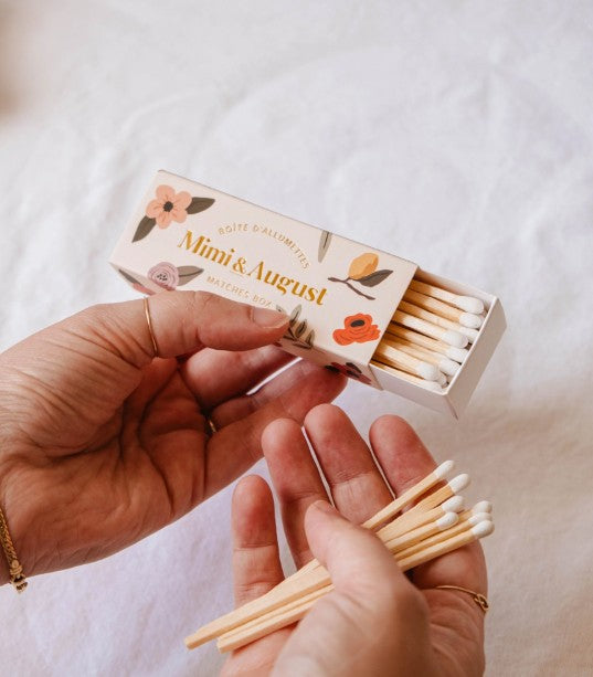 Person holding a box of Mimi & August matches on a white background