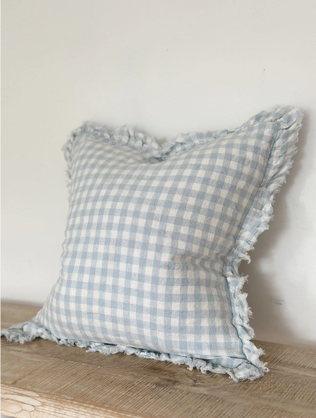 Blue and white checkered pillow with frayed edges on a wooden surface.