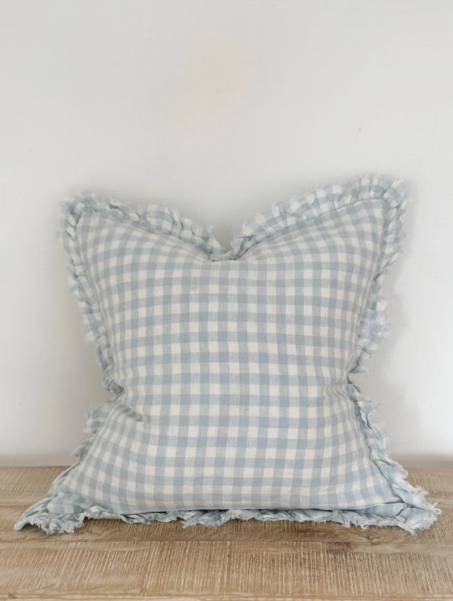 Blue and white checkered pillow with ruffled edges on a wooden surface.
