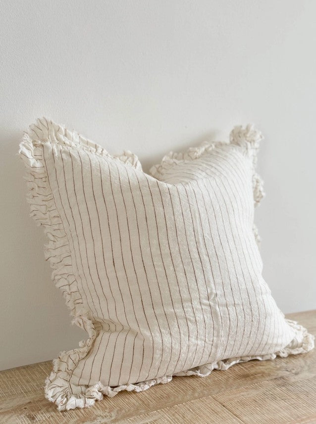 Textured pillow with ruffled edges on a wooden surface against a white wall