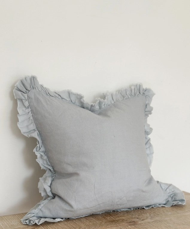 Gray pillow with ruffled edges on a light wooden floor against a white wall