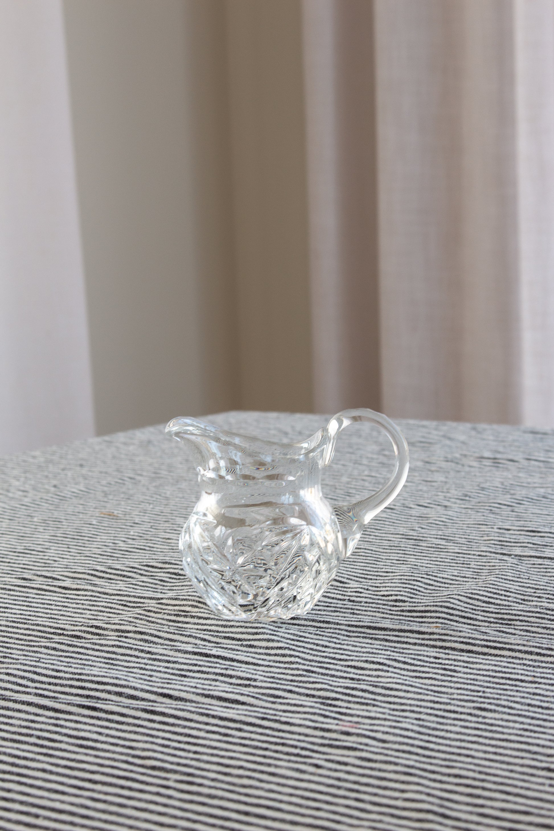 Clear glass pitcher on a textured surface with a neutral background