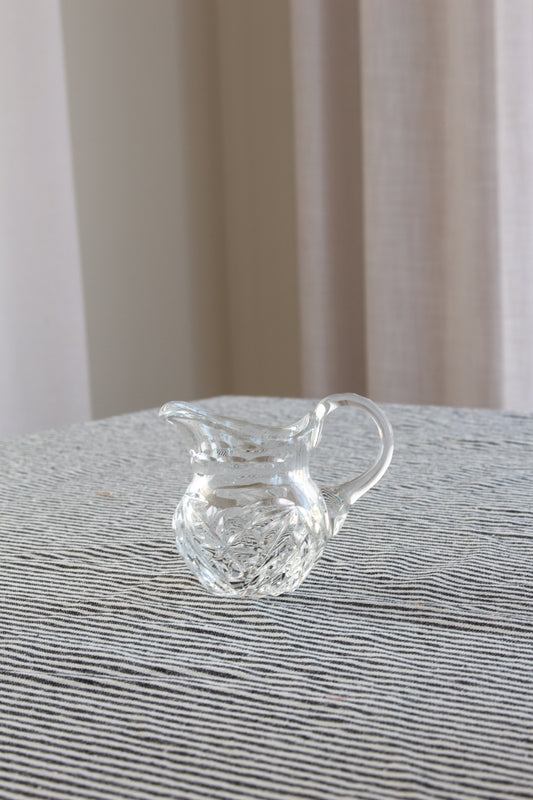 Clear glass pitcher on a textured surface with a neutral background