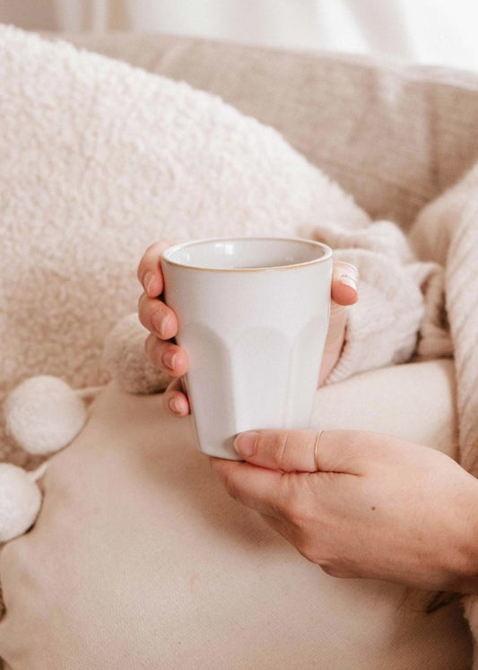 Person holding a white mug with a soft, cozy background