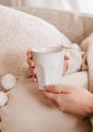 Person holding a white mug with a soft, cozy background