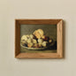 Framed still life painting of apples on a plate against a beige wall