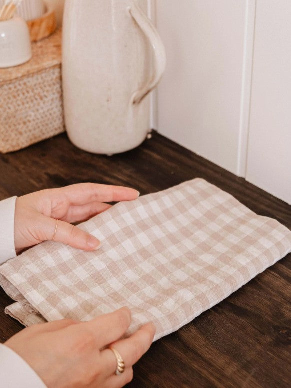 Person holding a checkered cloth on a wooden surface with a kitchen background