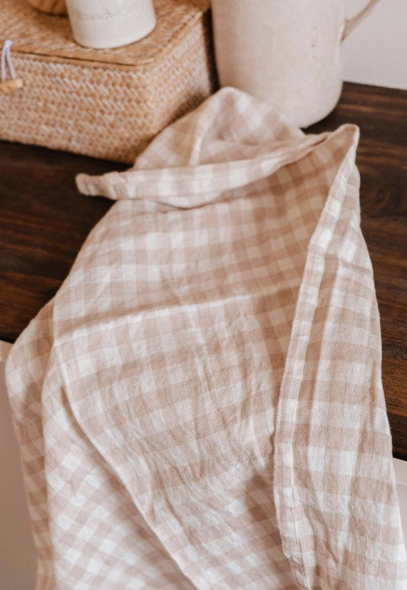 Beige checkered fabric draped over a surface with a woven basket and white container in the background.