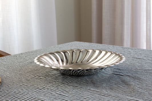 Silver decorative bowl on a striped tablecloth with a neutral background